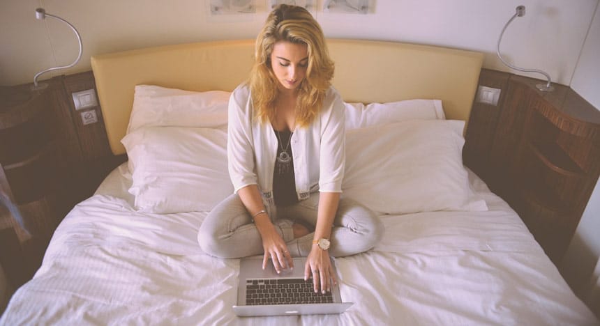 Vue du dessus d'une jeune femme assise en tailleur dans son lit et manipulant un ordinateur portable devant elle
