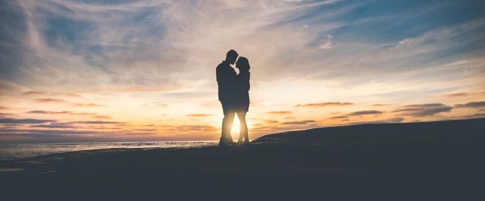 Vue de loin d'un couple debout, à contre-jour, s'embrassant devant un coucher de soleil