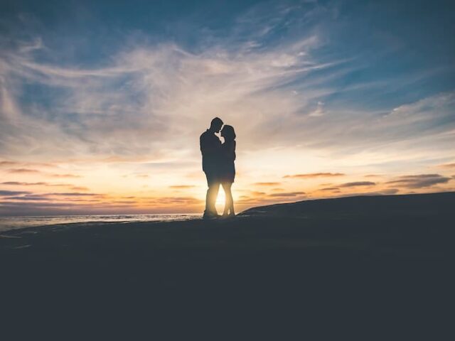 Vue de loin d'un couple debout, à contre-jour, s'embrassant devant un coucher de soleil