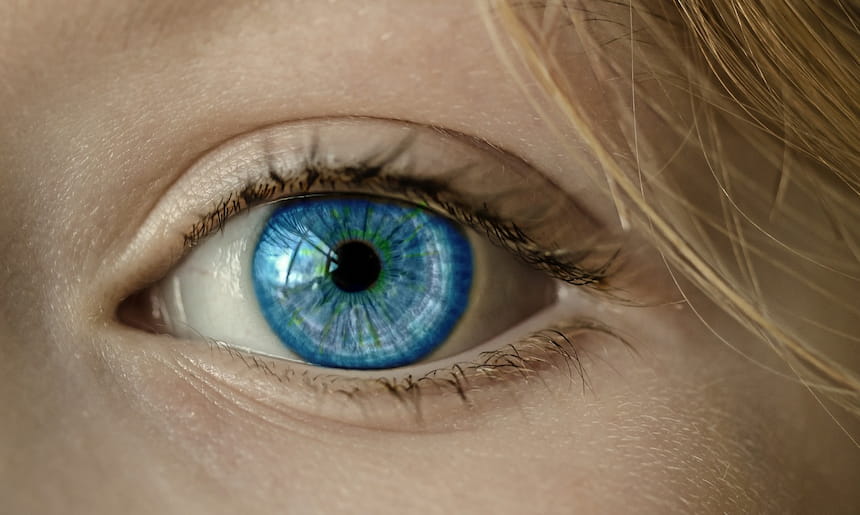 Photo en gros plan d'un œil de femme blanche, de couleur bleue. On aperçoit des mèches de cheveux blonds à droite de l'oeil.